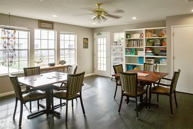 A well-lit dining area with tables and chairs, surrounded by bookshelves and large windows allowing ample natural light.