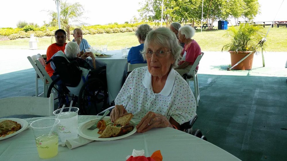 An elderly woman sitting at a table enjoying a meal outdoors.