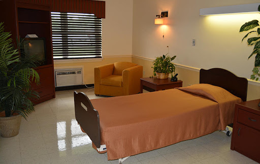 A clean and simple hospital room featuring a patient bed, an armchair, and natural light from the window.