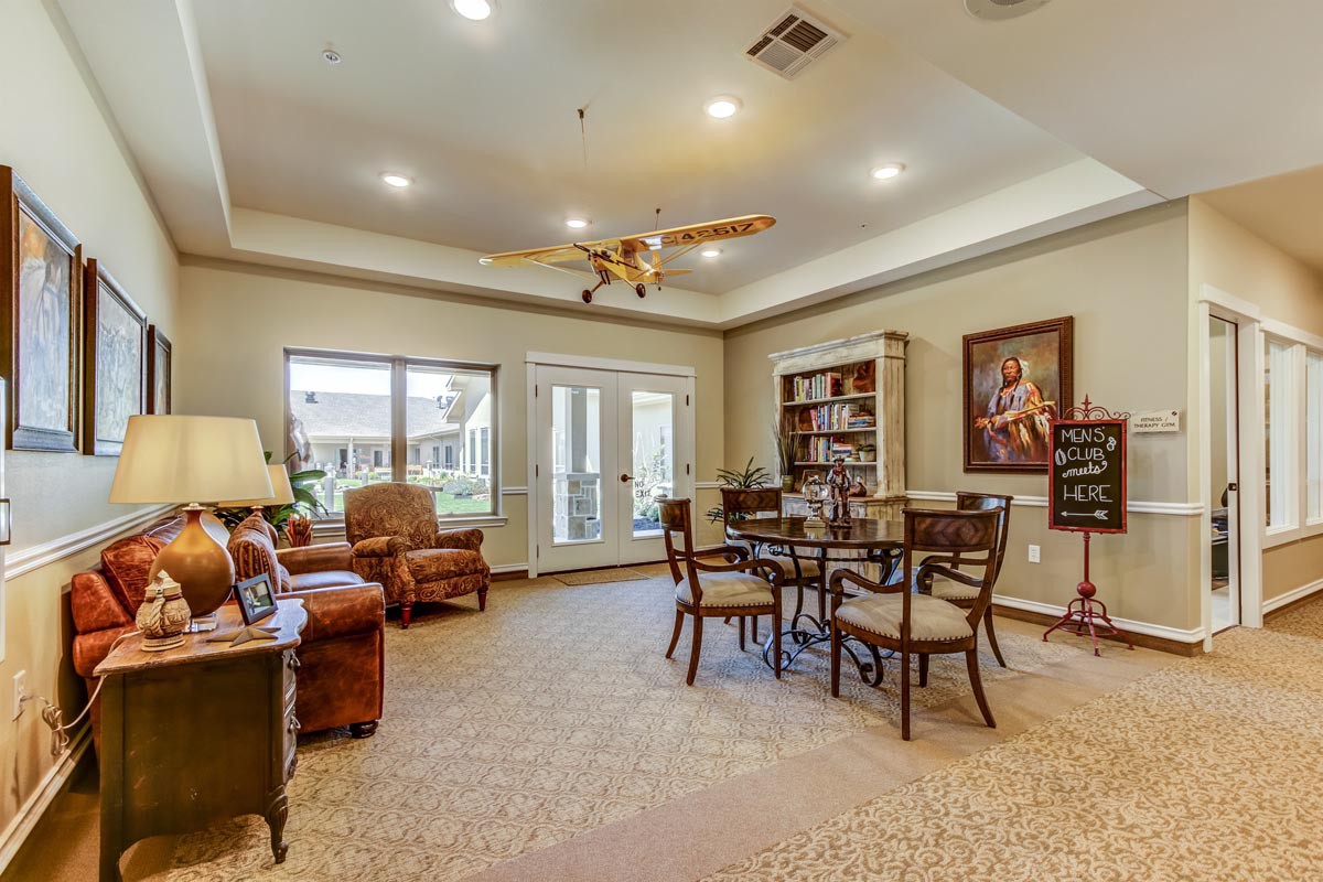 A cozy living room featuring comfortable seating, a central table with chairs, bookshelves, and decorative elements.