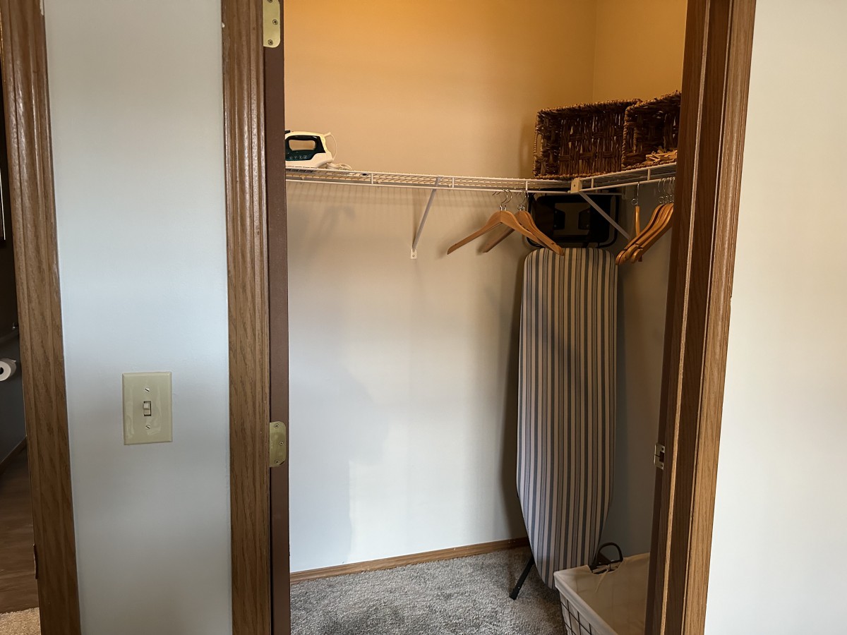 An empty closet with hangers and an ironing board.
