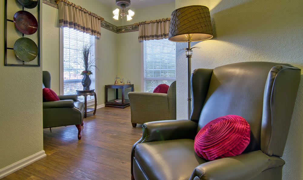 A cozy living room with comfortable armchairs, a floor lamp, and abundant natural light streaming through large windows.