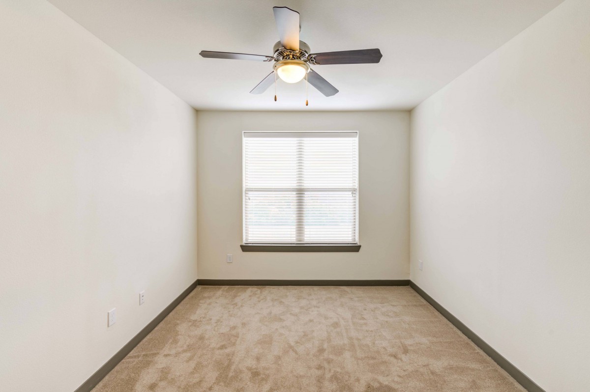 An empty room with a carpeted floor, ceiling fan, and a large window.