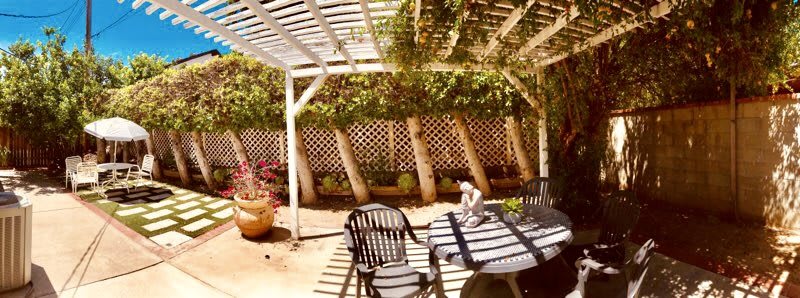 A sunny patio with a pergola, outdoor seating, and lush greenery.