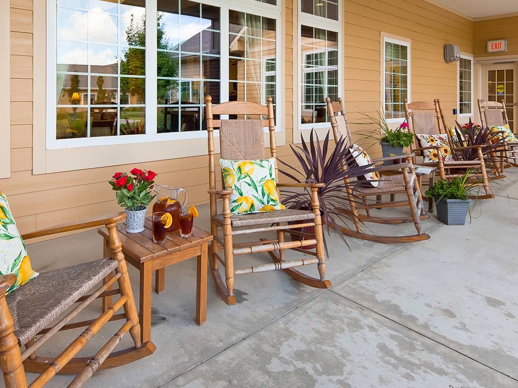 A cozy porch setup with rocking chairs, a small table with flowers and beverages, and decorative cushions.