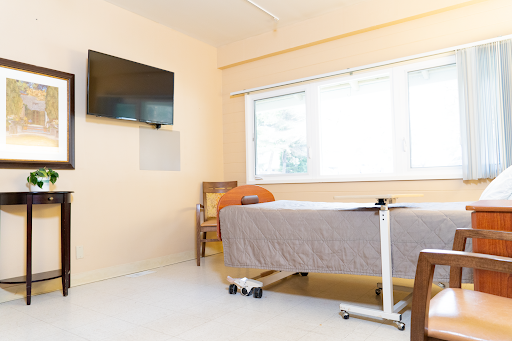 A neat and well-lit hospital room featuring a bed, a television, and a comfortable chair by the window.