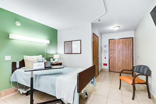 A well-lit hospital patient room featuring a bed, a chair, and essential medical furnishings.
