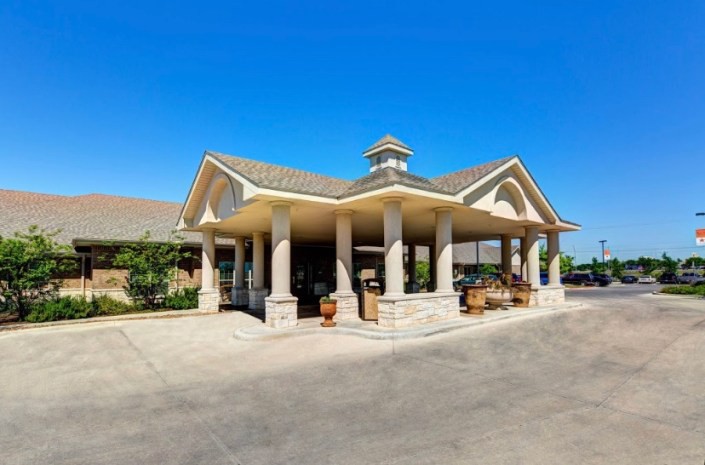 A building entrance with columns and a gabled roof under a clear blue sky.