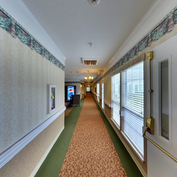 A long indoor hallway with carpeted flooring and large windows.