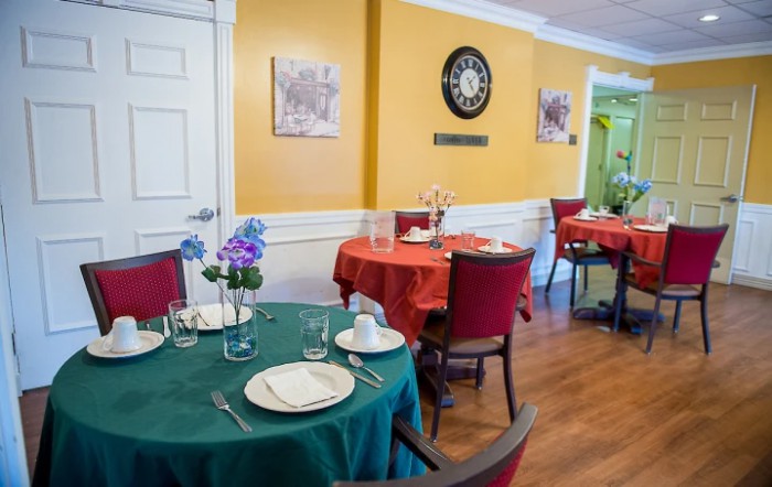 A cozy restaurant interior with round tables set for dining, adorned with colorful tablecloths and floral centerpieces.