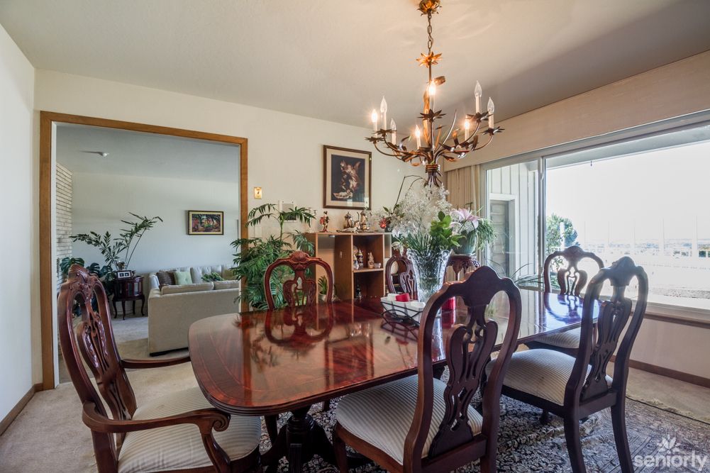 A cozy dining room with a wooden table and chairs, decorated with plants and illuminated by a chandelier.