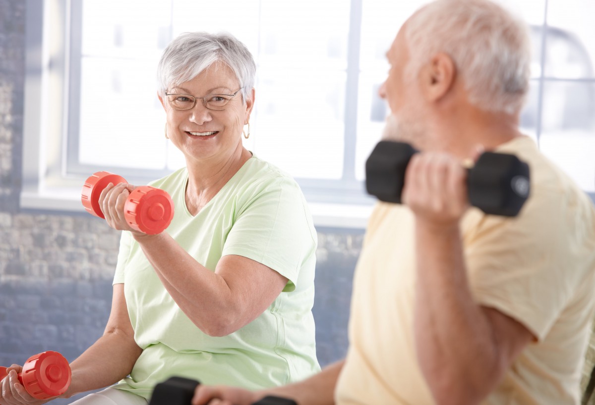 Two seniors lifting dumbbells while smiling at each other during a workout.