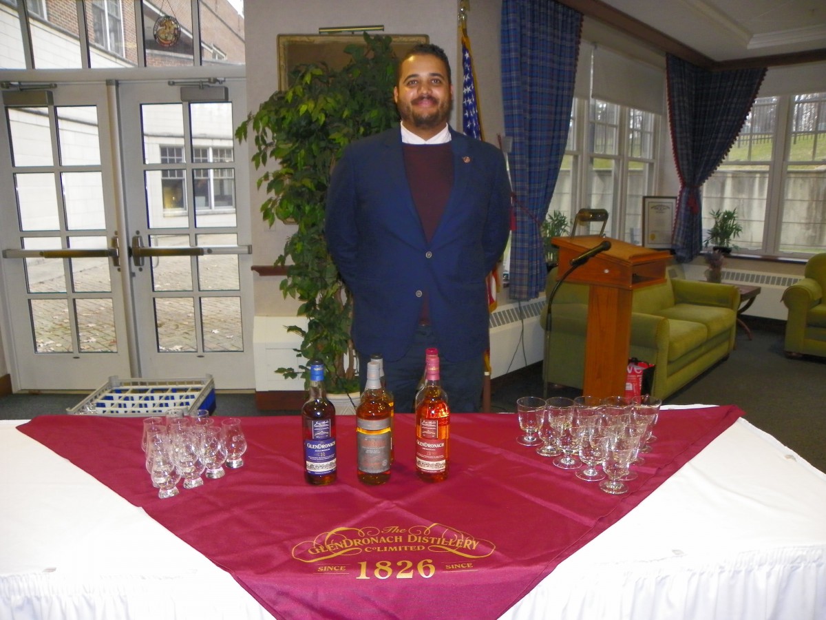 A person stands behind a table displaying various bottles and glasses at an indoor event.