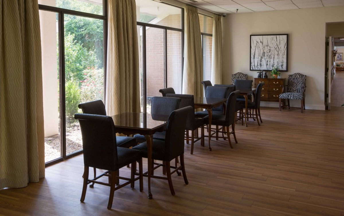 A quiet room with tables and chairs near large windows, allowing natural light to fill the space.