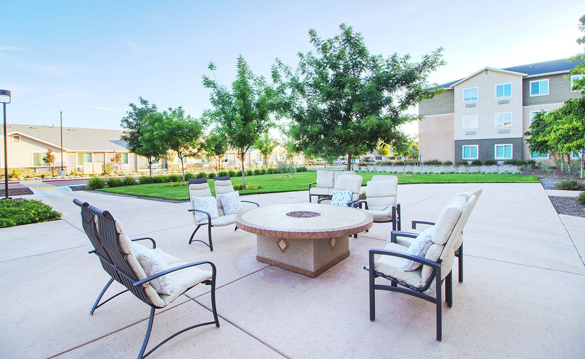 A patio with cushioned chairs arranged around a fire pit, set in a landscaped garden.