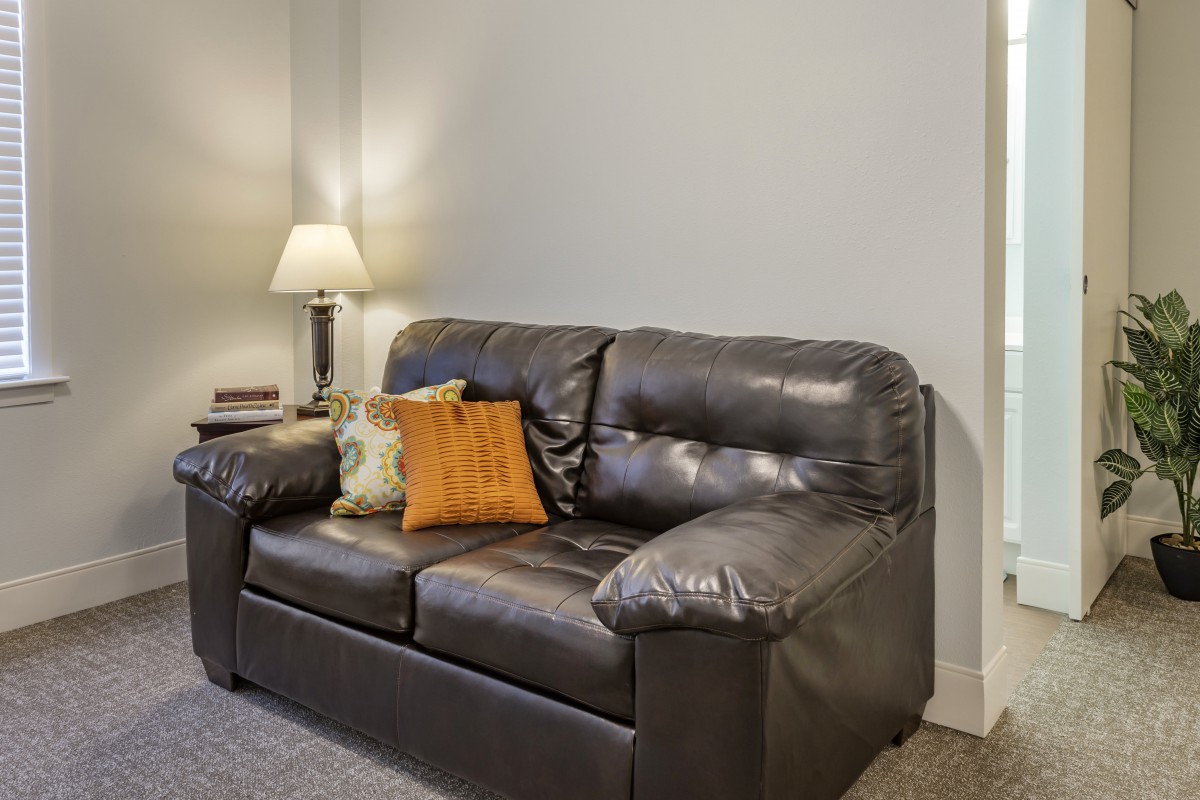 A cozy living room setup featuring a leather sofa with colorful cushions and a nearby lamp.