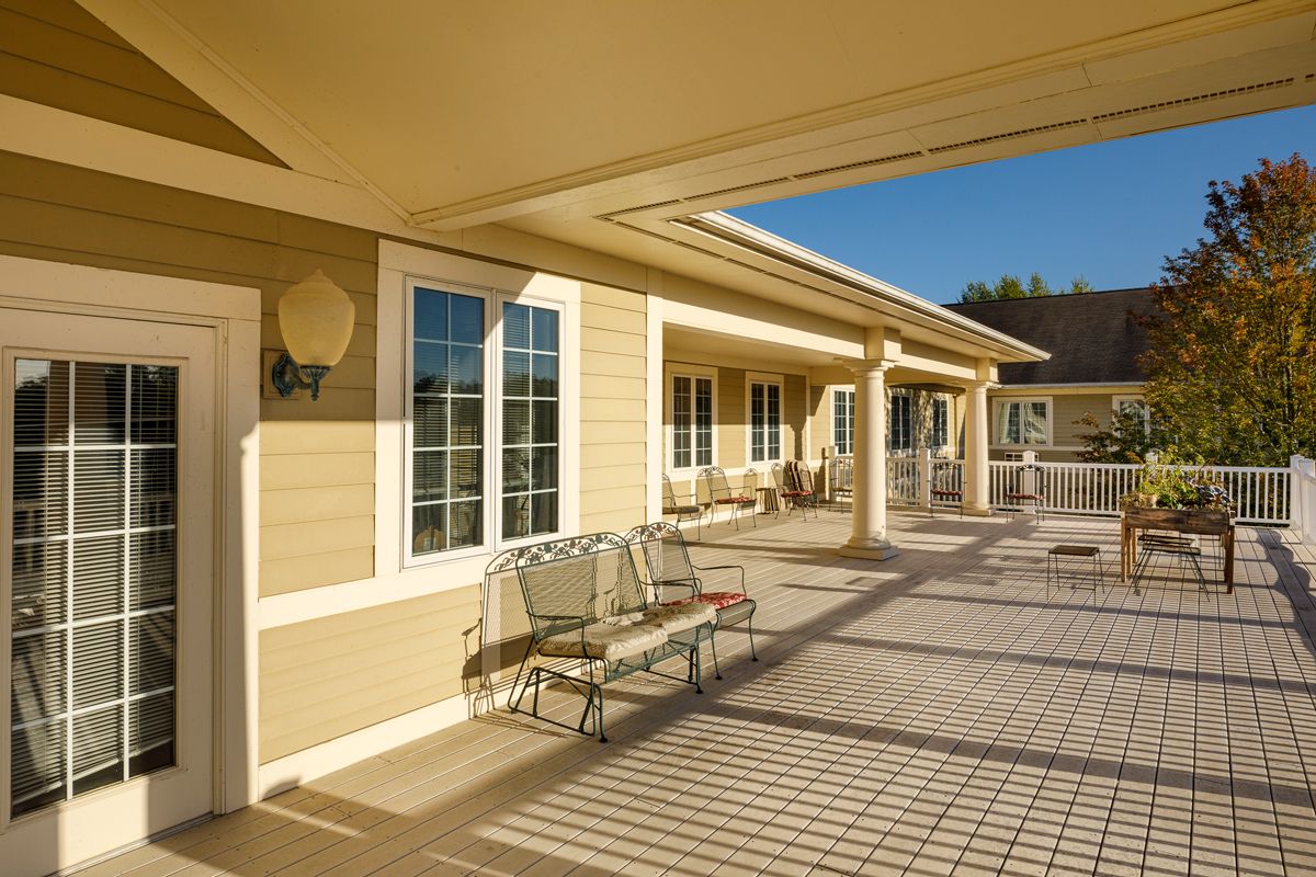 A sunny patio area with chairs, attached to a building with cream-colored siding.