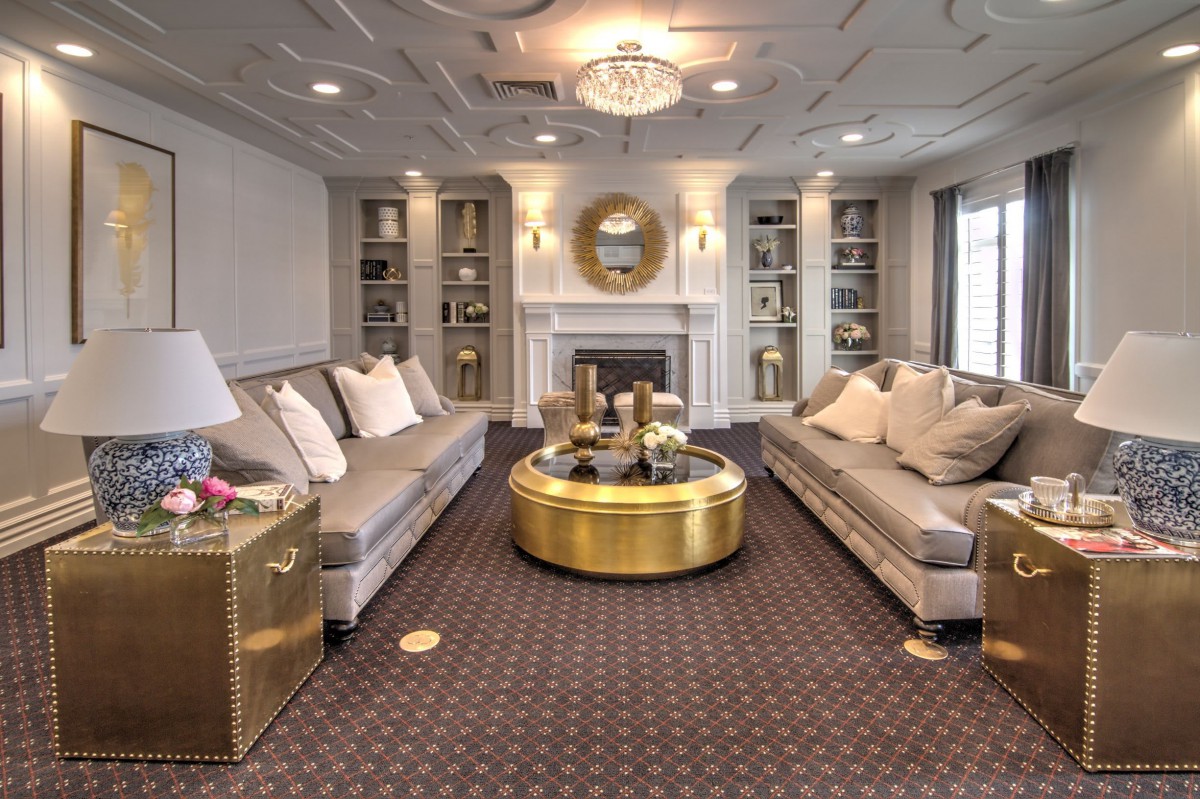 Luxurious living room with elegant sofas and a central gold coffee table, featuring a chandelier and fireplace.