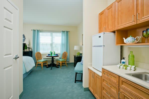 A cozy hotel room featuring a bed, kitchenette, and seating area with a table and chairs by the window.