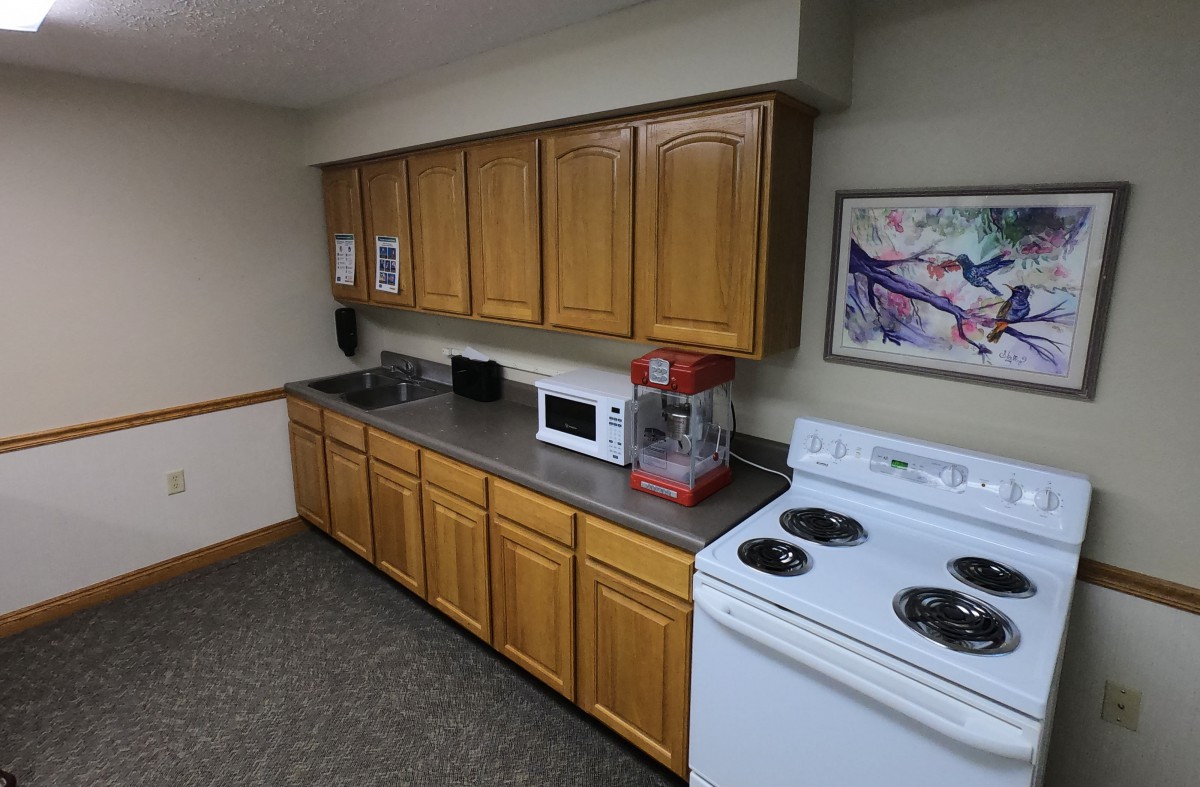 A small kitchen area with wooden cabinets, a microwave, stove, and a popcorn machine on the countertop.