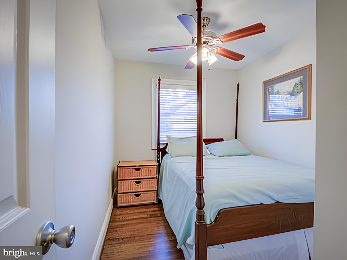 A cozy bedroom with a four-poster bed, ceiling fan, and wooden floors.