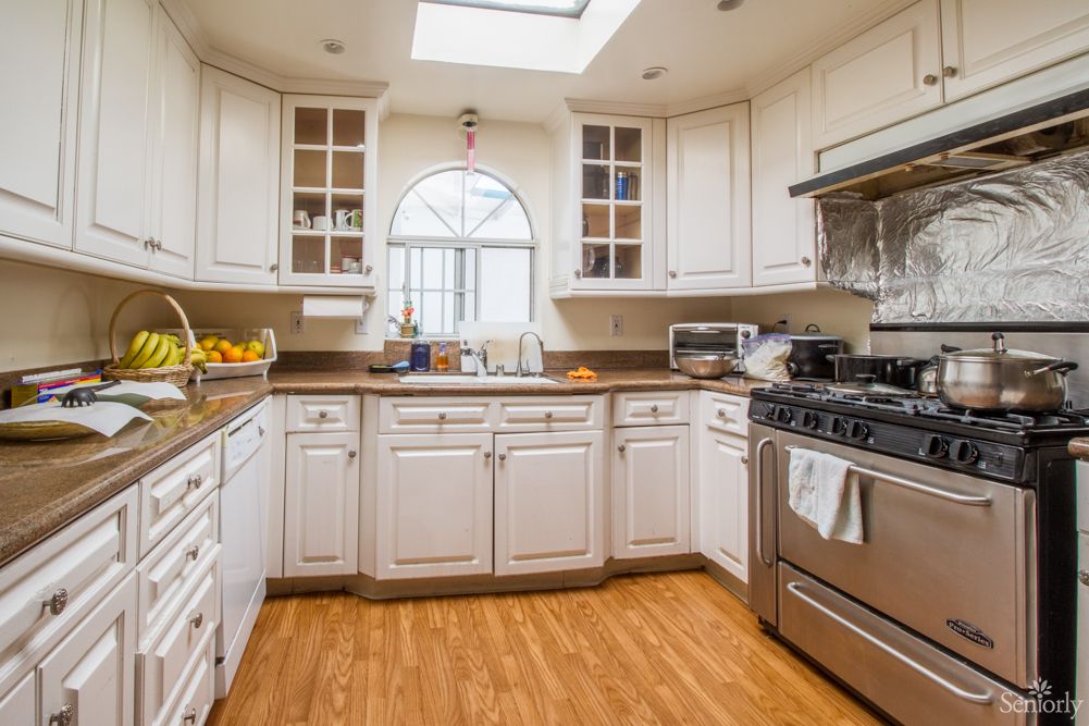 A modern kitchen with white cabinets, a stainless steel stove, and a wooden floor.