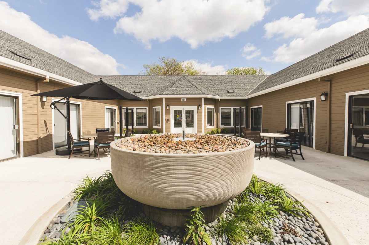 A serene courtyard featuring a large stone fountain surrounded by a well-maintained landscape and a cozy building.