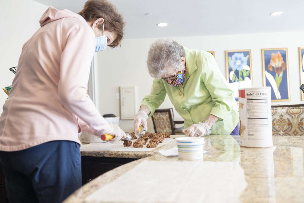 Two people, wearing masks, are preparing food together indoors, engaging in community service or volunteering.