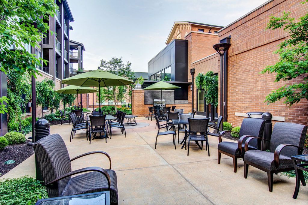 A well-furnished outdoor patio area with tables, chairs, and umbrellas set against a brick building.