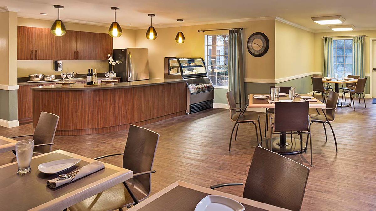 A modern cafe interior with a dining area, featuring tables and chairs, and a service counter.
