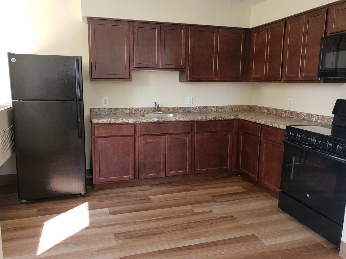 Modern kitchen with wooden cabinets and flooring, featuring a refrigerator and stove.