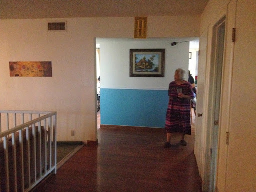A cozy indoor hallway featuring a blue wall and an elderly woman standing thoughtfully.
