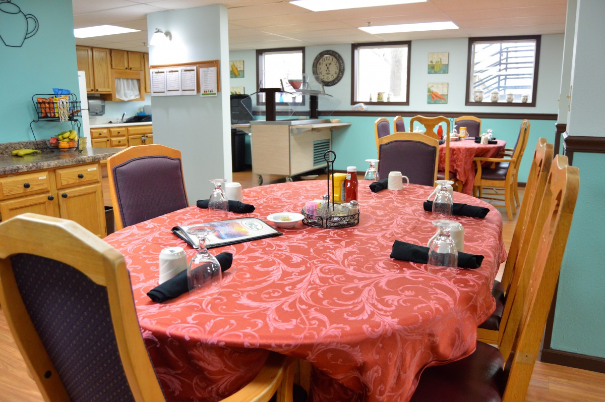 A dining room with a neatly set table, featuring a red tablecloth and arranged black napkins.