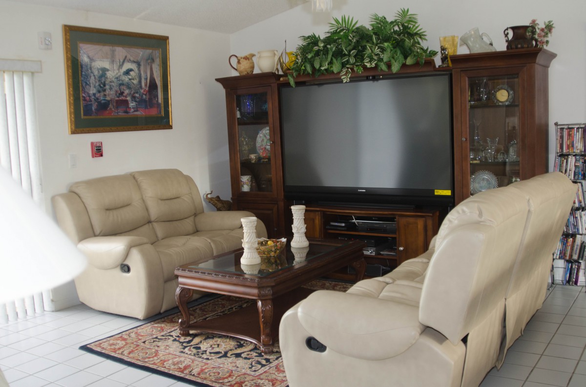A cozy living room featuring beige leather sofas, a wooden coffee table, and a large flat-screen TV surrounded by decorative elements.