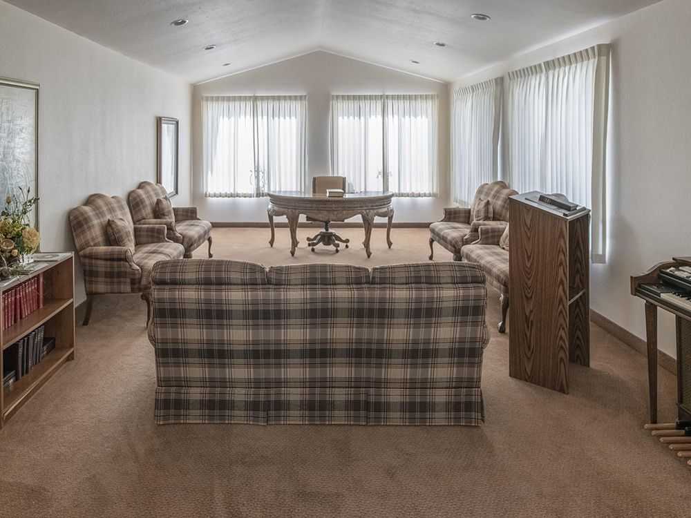 A spacious living room with a plaid sofa, multiple armchairs, and a desk near large windows with curtains.