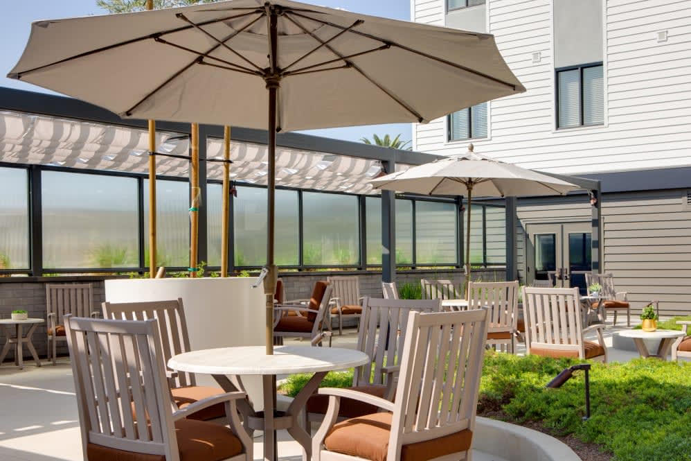A sunny patio with tables and chairs shaded by large umbrellas.