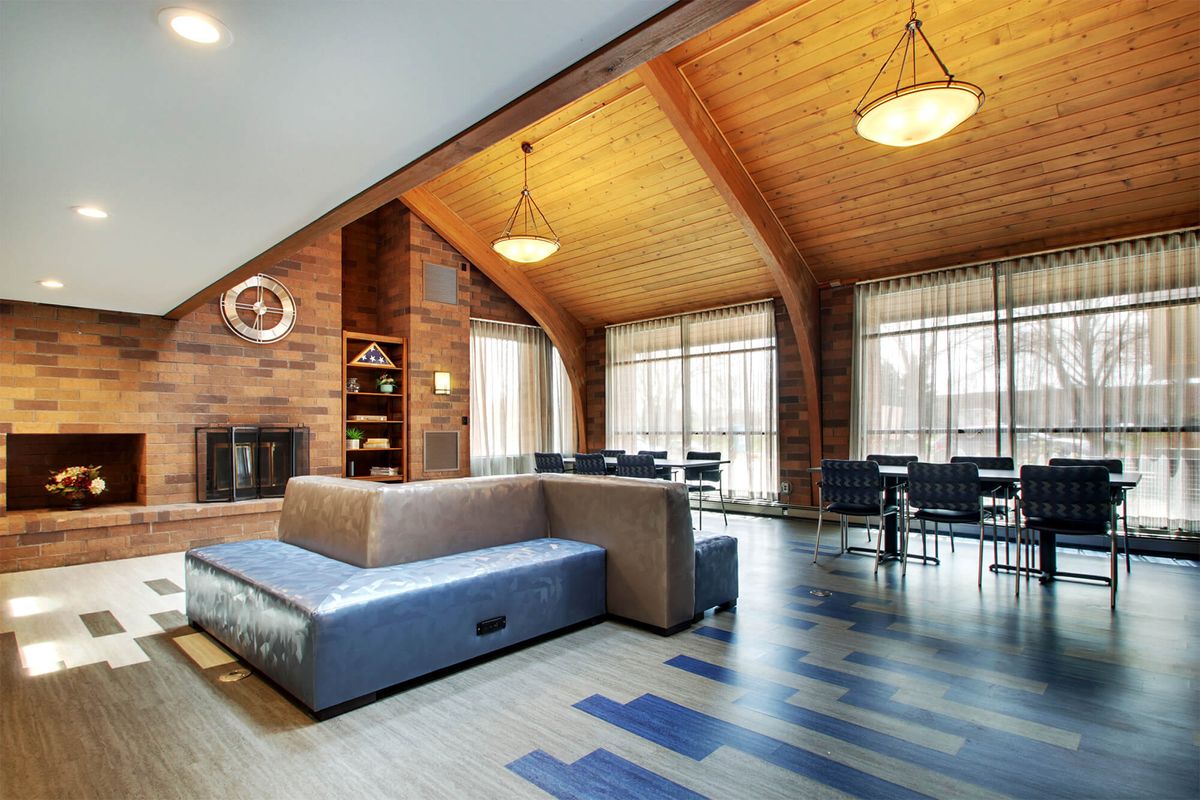 A modern living room with a high wooden ceiling, featuring a cozy sofa, fireplace, and dining area with large windows.