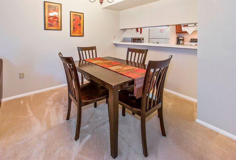 A dining room with a wooden table and four chairs, featuring colorful wall art.