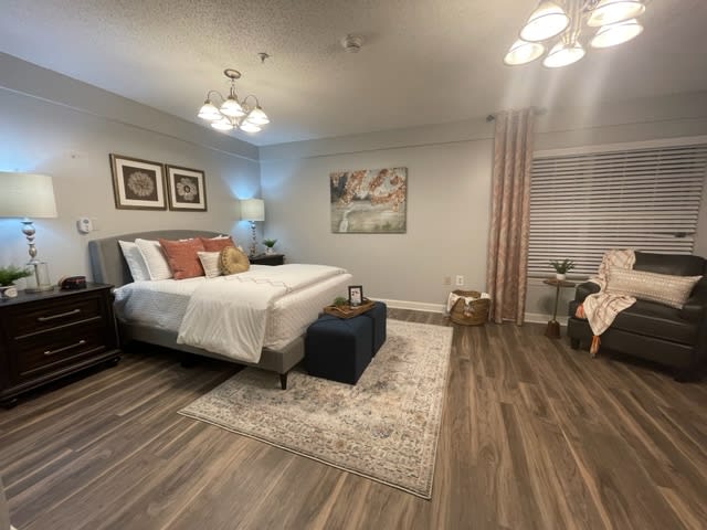 A modern and well-decorated bedroom with wood flooring, featuring a large bed, stylish lamps, and wall art.