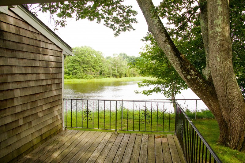 A peaceful view from a wooden deck overlooking a tranquil lake surrounded by lush greenery.