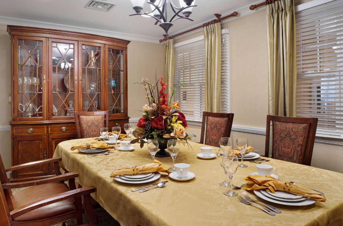 An elegantly set dining room with a flower centerpiece and a chandelier above the table.