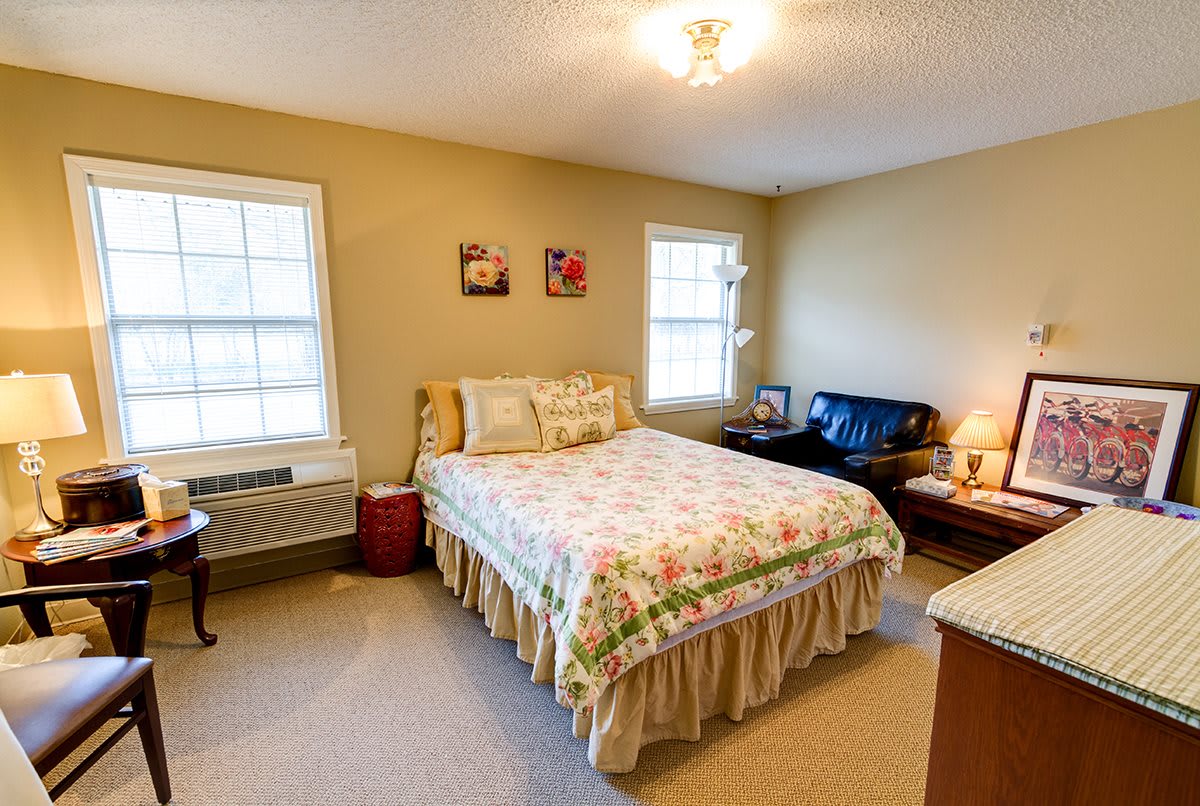 A cozy bedroom with a bed, two windows, a lamp, and decorative elements.