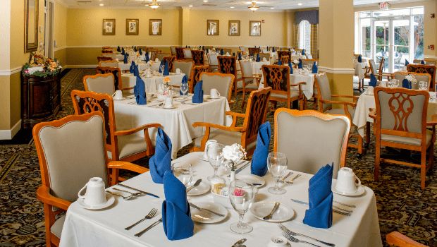 A neatly arranged dining area with tables set for a formal meal, featuring blue napkins and elegant decor.