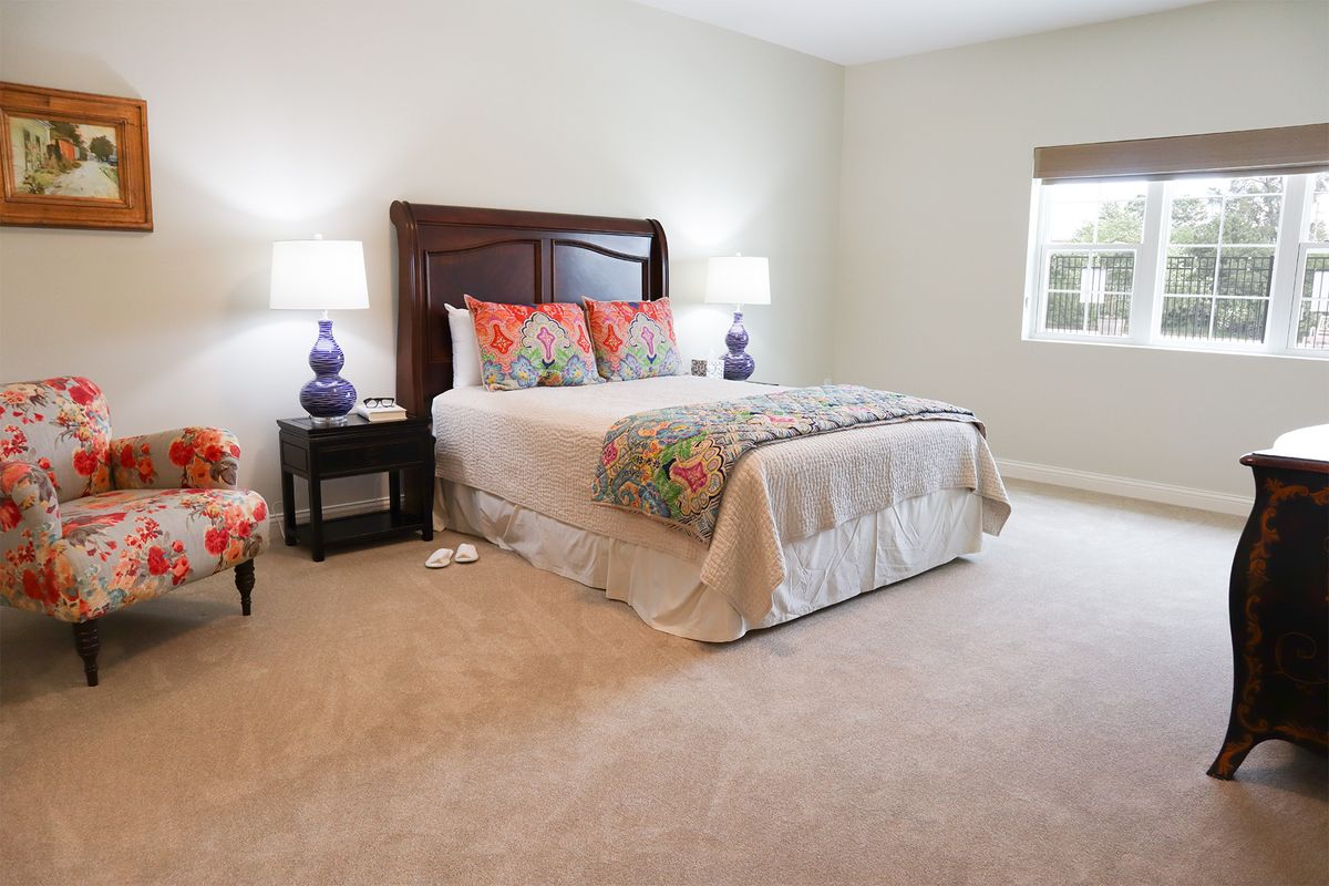 A cozy bedroom with a neatly made bed, adorned with colorful pillows and flanked by matching lamps on bedside tables.