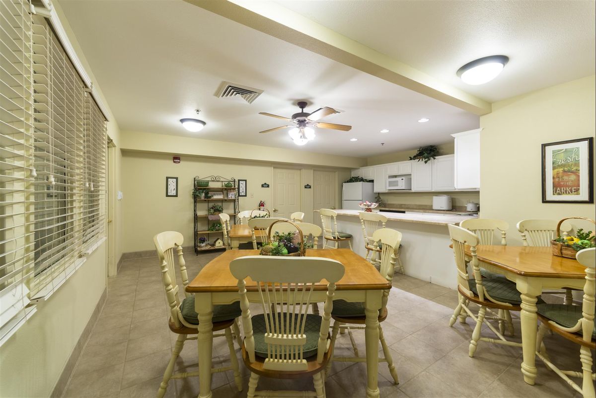 A spacious dining area connected to a kitchen, featuring wooden tables and chairs under soft lighting.