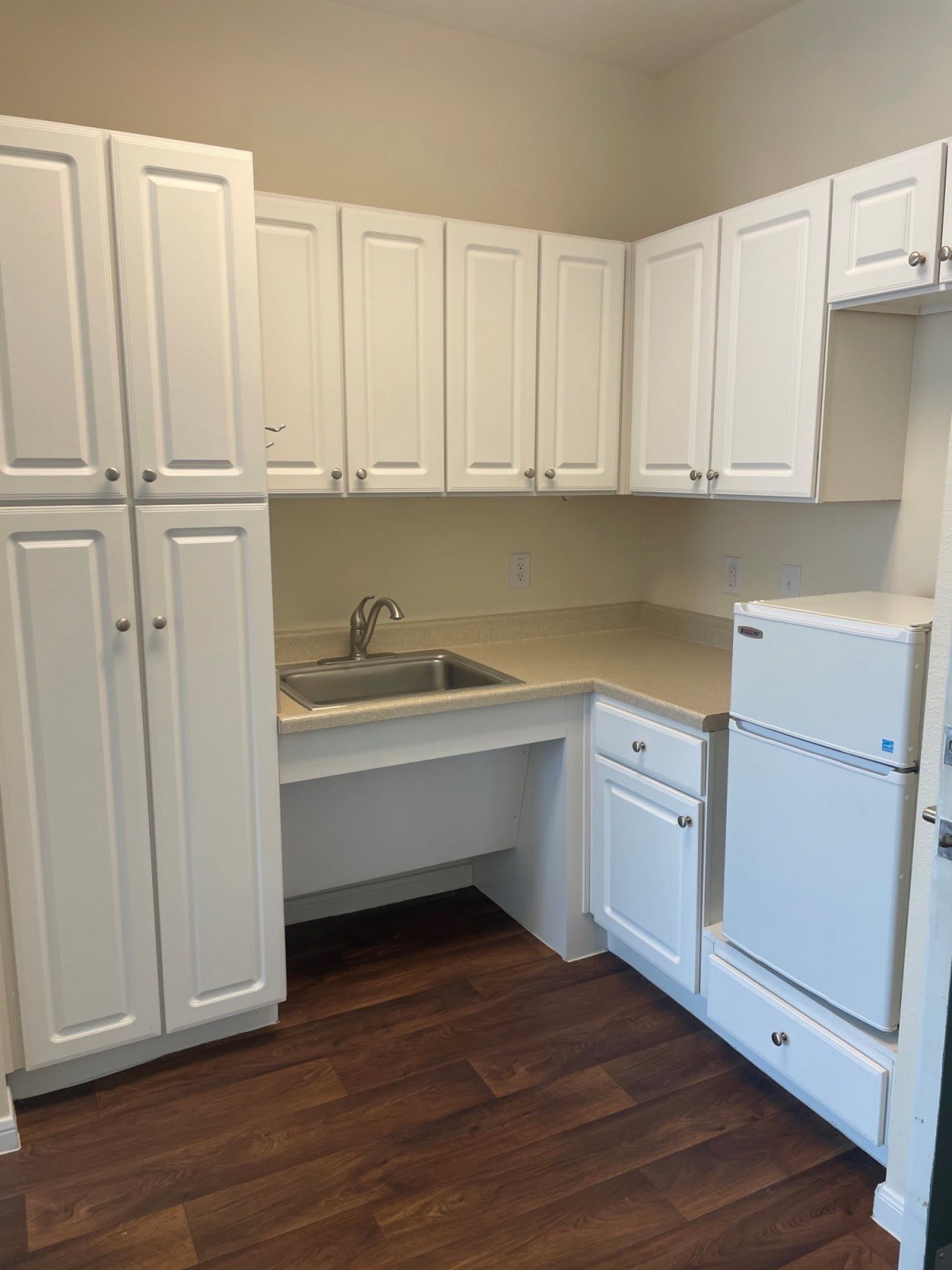 A compact kitchen with white cabinets, a small sink, and a refrigerator.