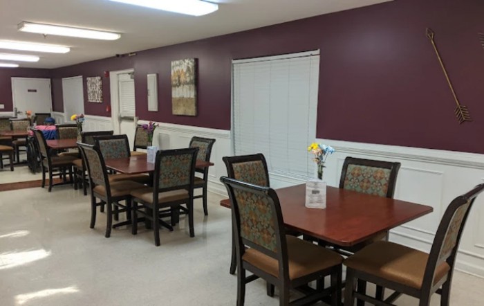 An empty dining room with neatly arranged tables and chairs against a maroon wall.