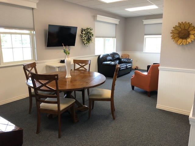 A cozy living room with a wooden dining table, chairs, a sofa, armchair, and a wall-mounted television.