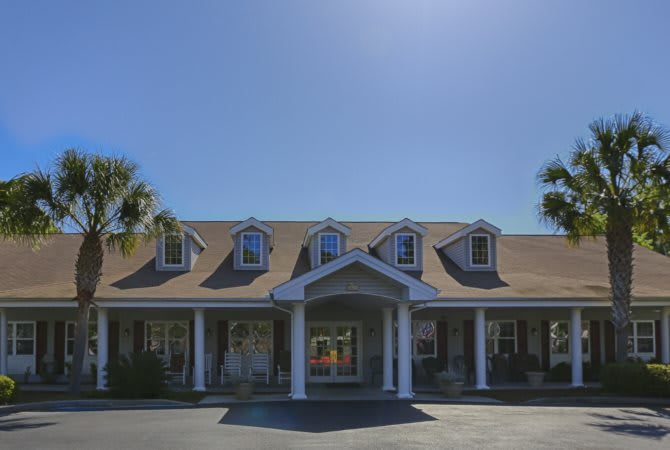 A sunny exterior view of a house with dormer windows and palm trees.