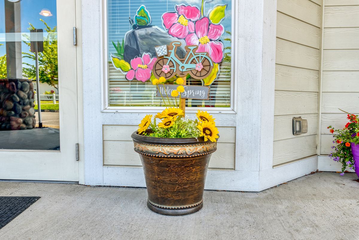 A decorative flower pot filled with sunflowers sits in front of a door with colorful window art.